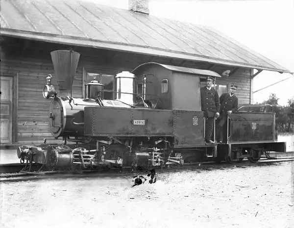 Foto av ett ånglok med lokförare. På lokets långsida syns en skylt med