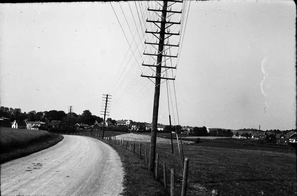 Trådrika telefonstolpar längs landsvägen till ett mindre samhälle i