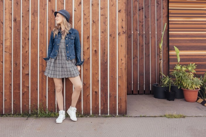Full-growth shot of a beautiful young girl in casual clothes posing on the background of a wooden fence in the countryside during a summer holiday. Student leave concept
