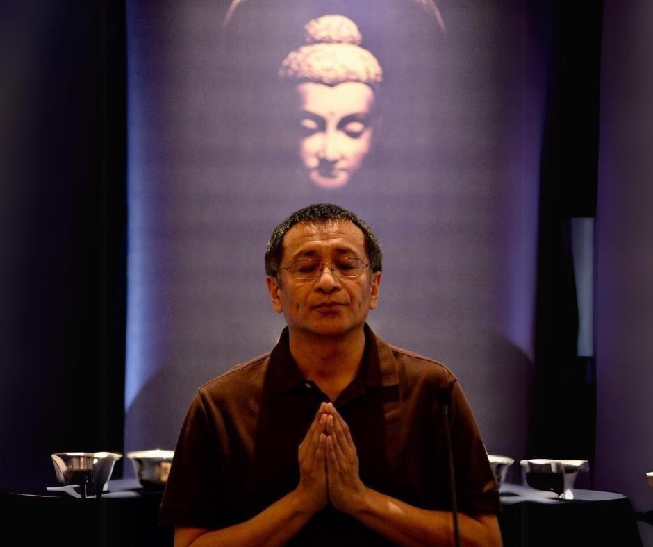 Dzogchen Ponlop Rinpoche praying, with the face of Buddha Shakyamuni on a backdrop overhead