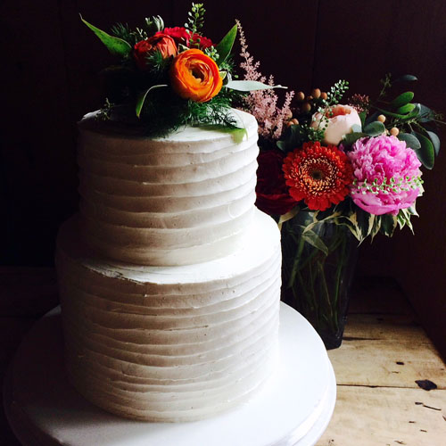Beautiful two tier cake in buttercream adorned with a colourful flower bouquet as topper