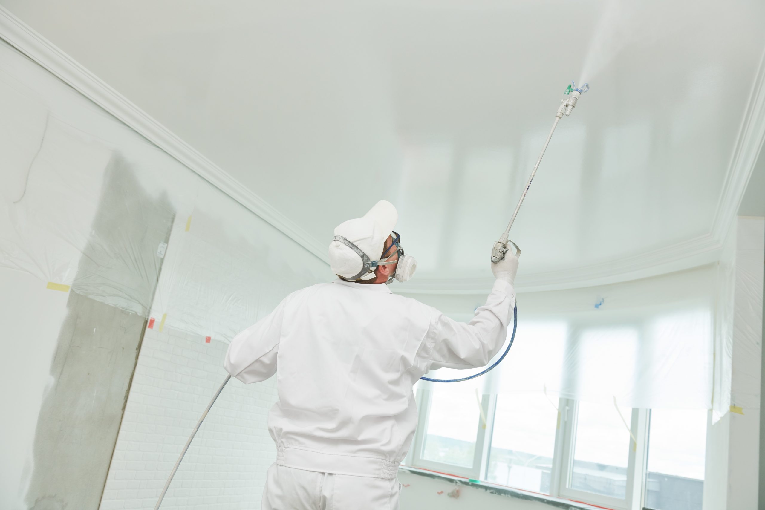 Painter worker with airless painting sprayer covering ceiling surface