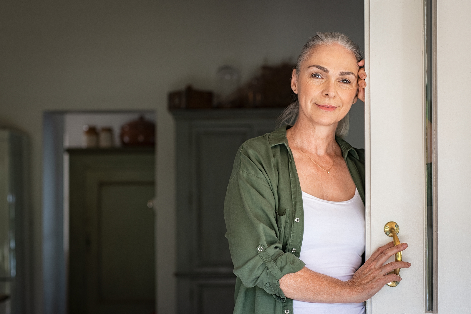 Portrait of senior woman leaning against door at home and lookin