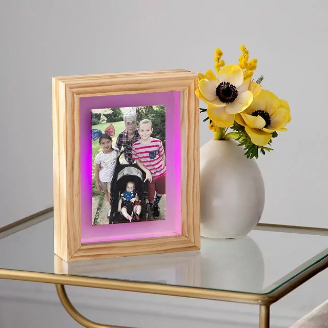 Long Distance Friendship Frame from UncommonGoods. The perfect quality time love language gift for long distance partners, friends, and family. The frame is made of a light wood, and has a glowing pink ring around a photo of a grandmother with three young grandchildren.