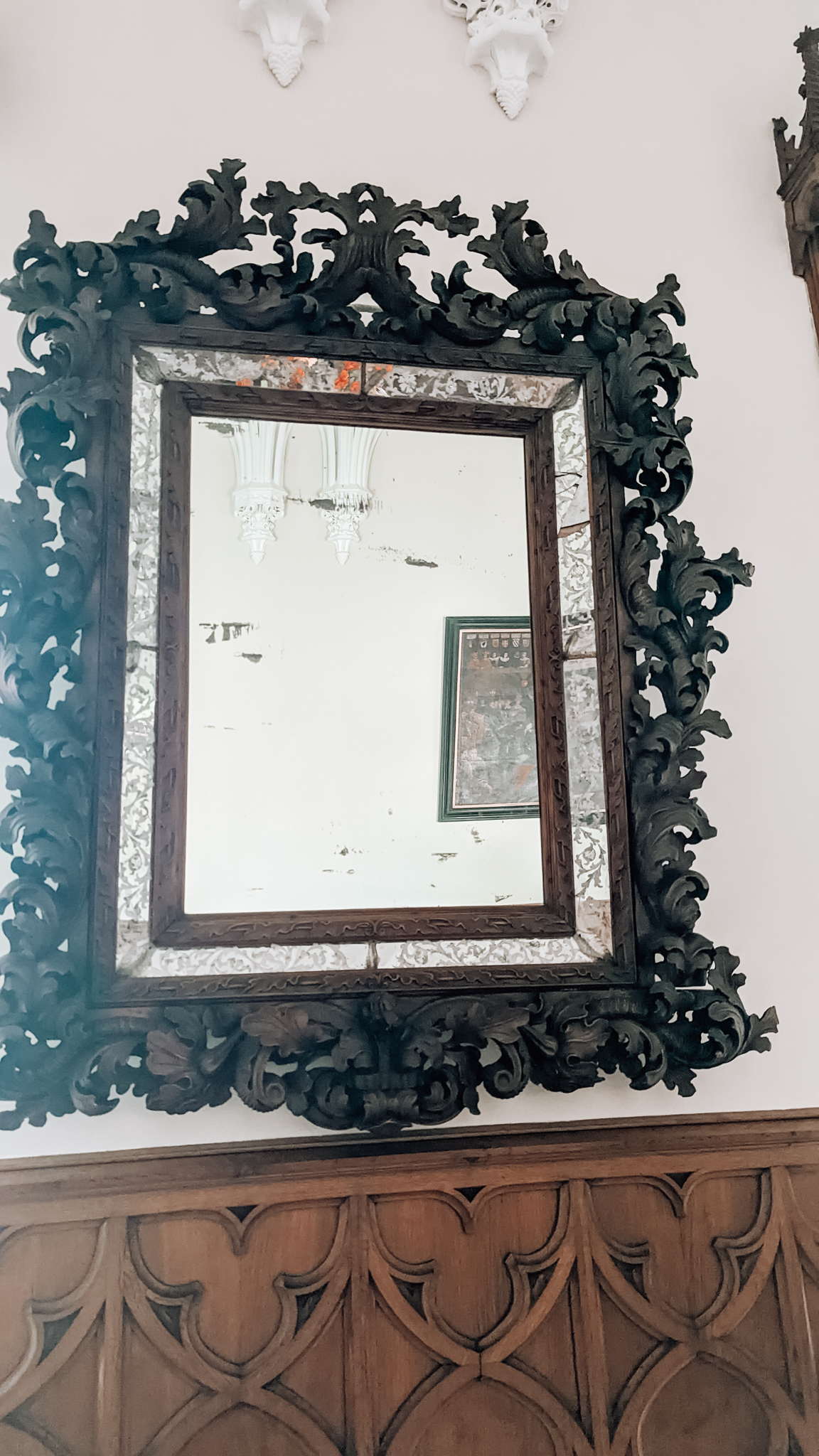 An old and dirty mirror hanging on the wall, with a black floral patterned frame. 
