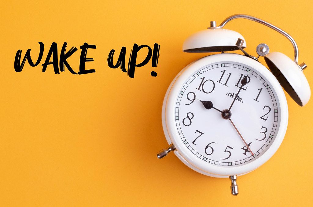 Alarm clock with handwritten text Wake Up on yellow background