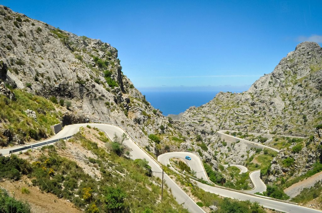 Car Driving down Serpentine Mountain Road with Blue Sky and Sea View in