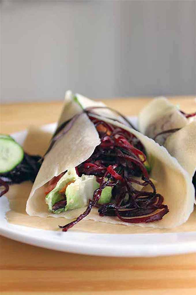 A close up vertical image of a vegetarian wrap set on a white plate on a wooden surface.