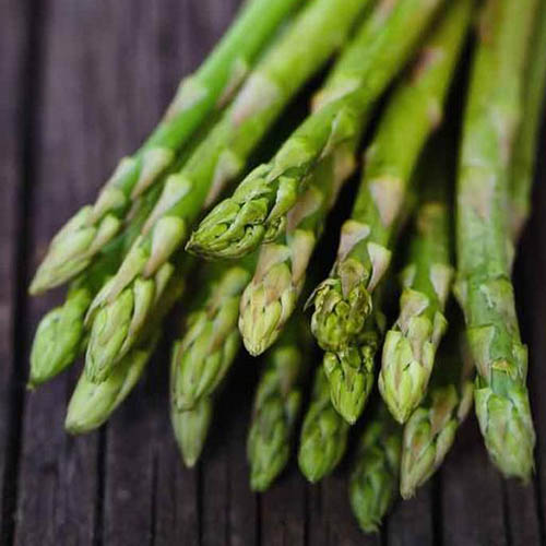 A close up of freshly harvested asparagus spears set on a wooden surface.