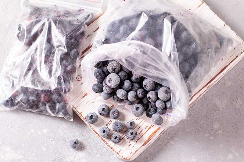 A close up horizontal image of two plastic bags filled with frozen fruits set on a wooden surface.