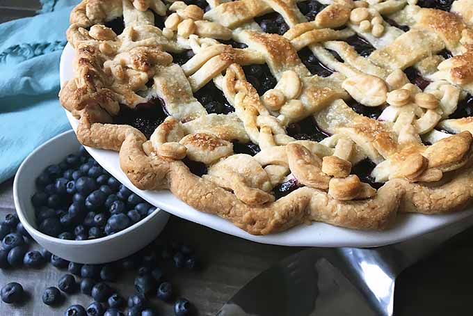 A horizontal image of a freshly baked blueberry pie set on a wooden surface.