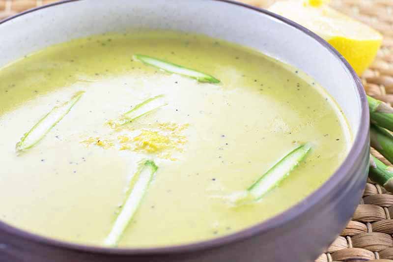 A close up horizontal image of freshly prepared cream of asparagus soup set on a wicker tablemat.