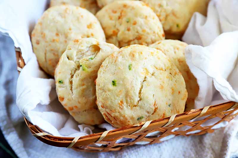 A close up horizontal image of freshly baked sourdough biscuits in a wicker basket.