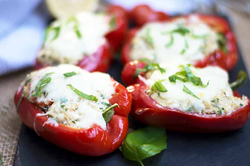 A close up horizontal image of homemade stuffed bell peppers set on a gray slate.
