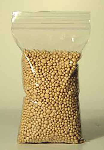 A close up vertical image of a small bag of fertilizer pellets isolated on a beige background.