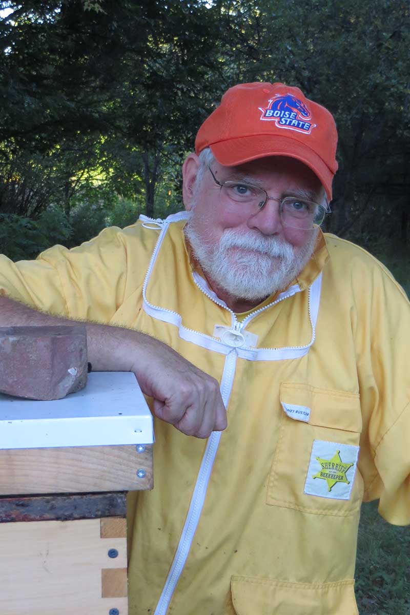 A close up vertical portrait of Kim Beeyard leaning against one of his hives.