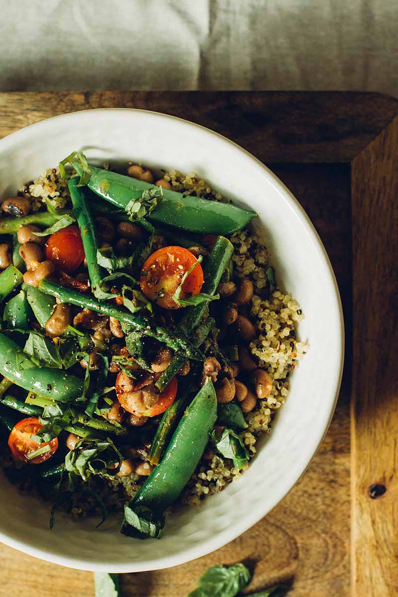 A close up vertical image of a bowl of homemade asparagus and snow pea salad set on a wooden surface.
