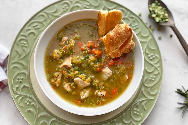 A horizontal image of a bowl of freshly made chicken split pea soup on a green decorative plate.