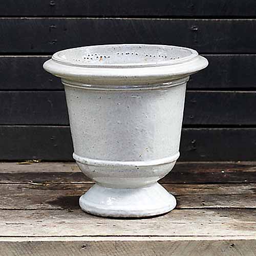 A close up square image of a ceramic urn set on a wooden surface.