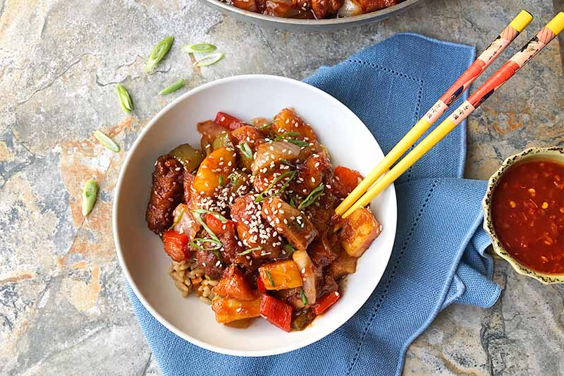 A close up of a bowl of sweet and sour pork set on a stone surface.