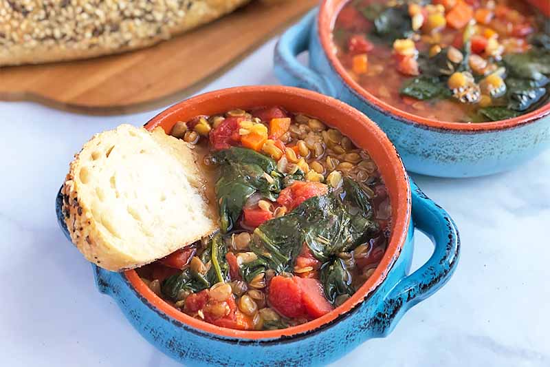 A close up horizontal image of freshly homemade Italian lentil soup in a blue ceramic bowl.