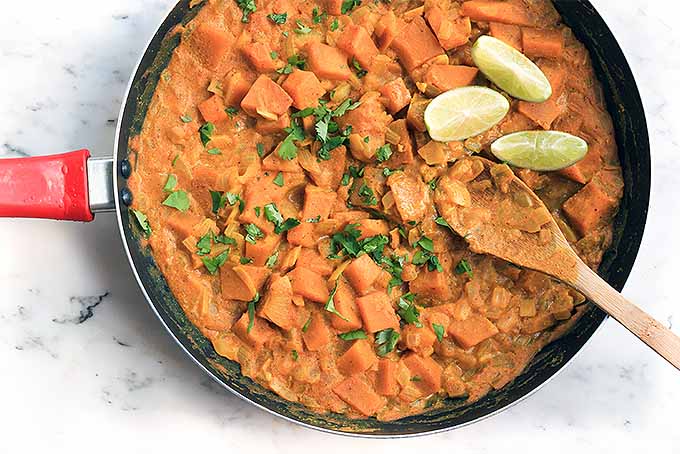 A close up of a freshly prepared pumpkin curry with herbs and lime wedges on the top.