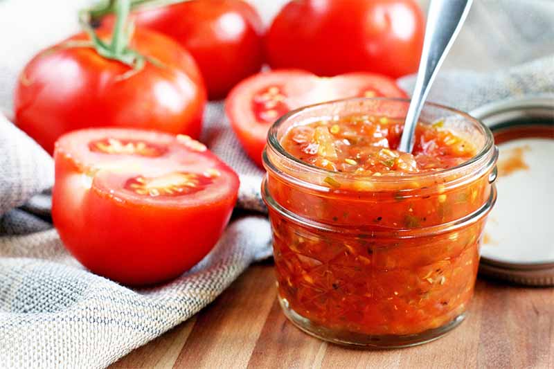 A close up horizontal image of a jar of fresh, homemade tomato jam set on a wooden surface.