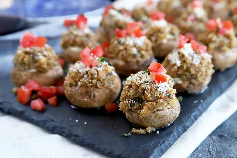 A close up horizontal image of a slate tray with rows of stuffed mushrooms.