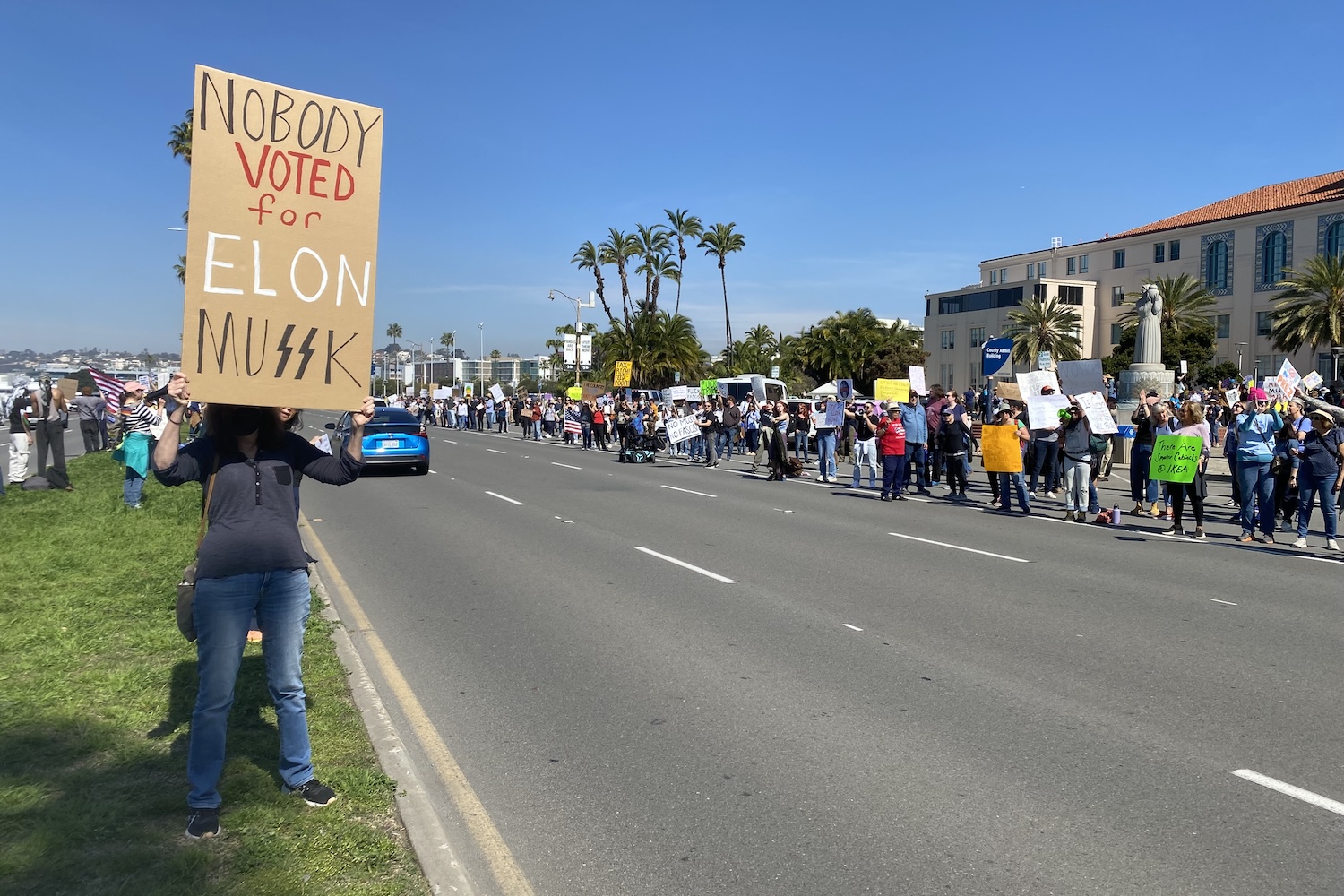 Protesters hold signs at a protest against Elon Musk and Donald Trump on Feb. 17, 2025 San Diego, California.