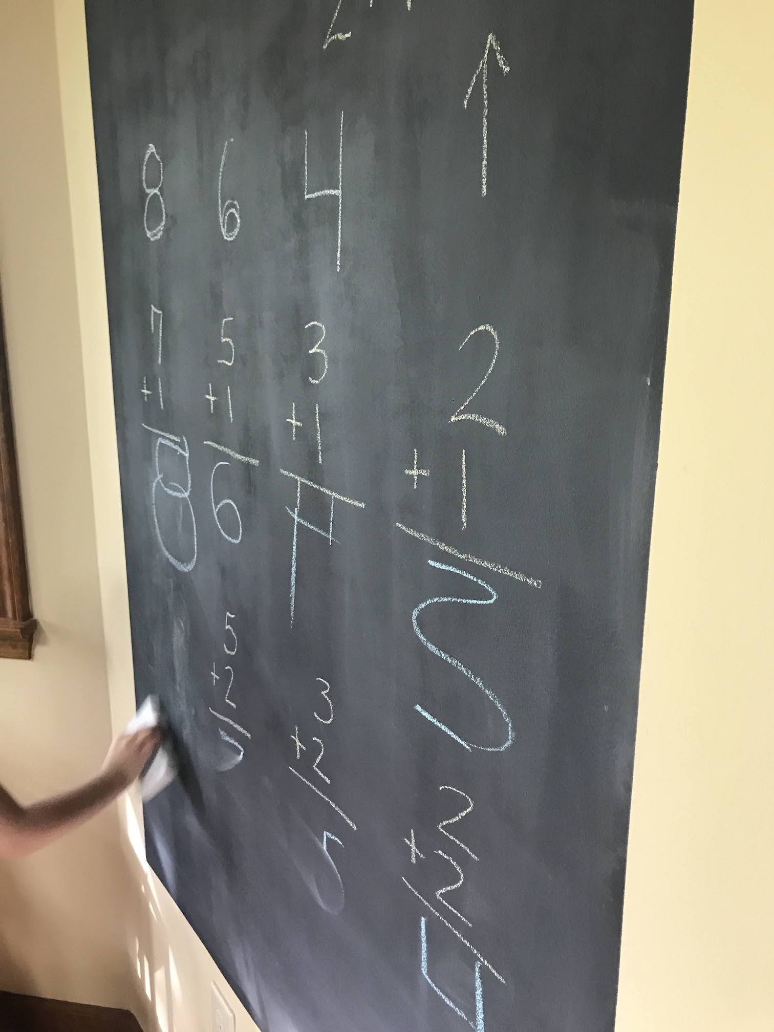 Two rows of simple addition problems written on black DIY chalkboard wall in white chalk