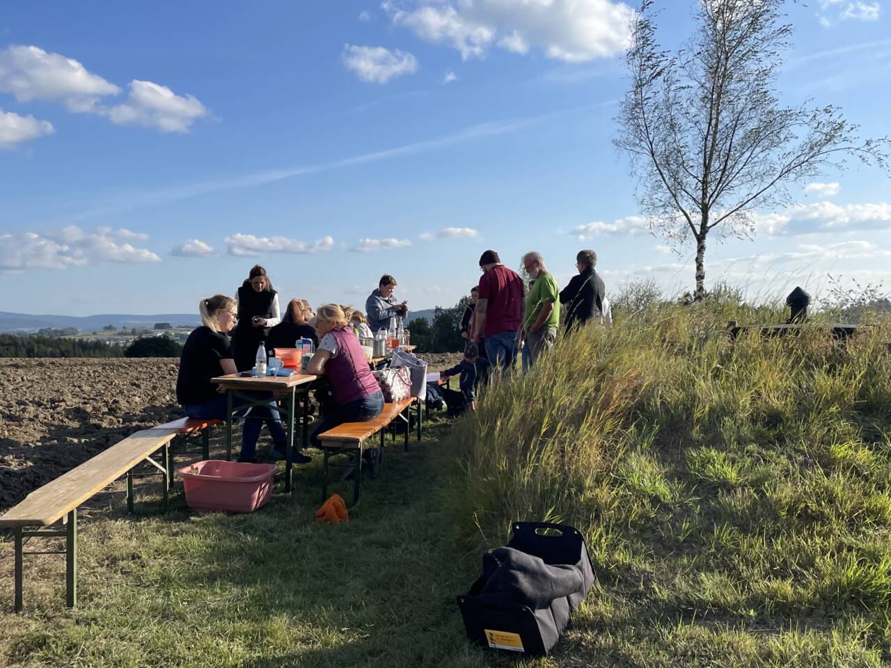 Kinder und Eltern sitzen zusammen auf Biergarnituren auf dem Kartoffelfeld und machen Pause.