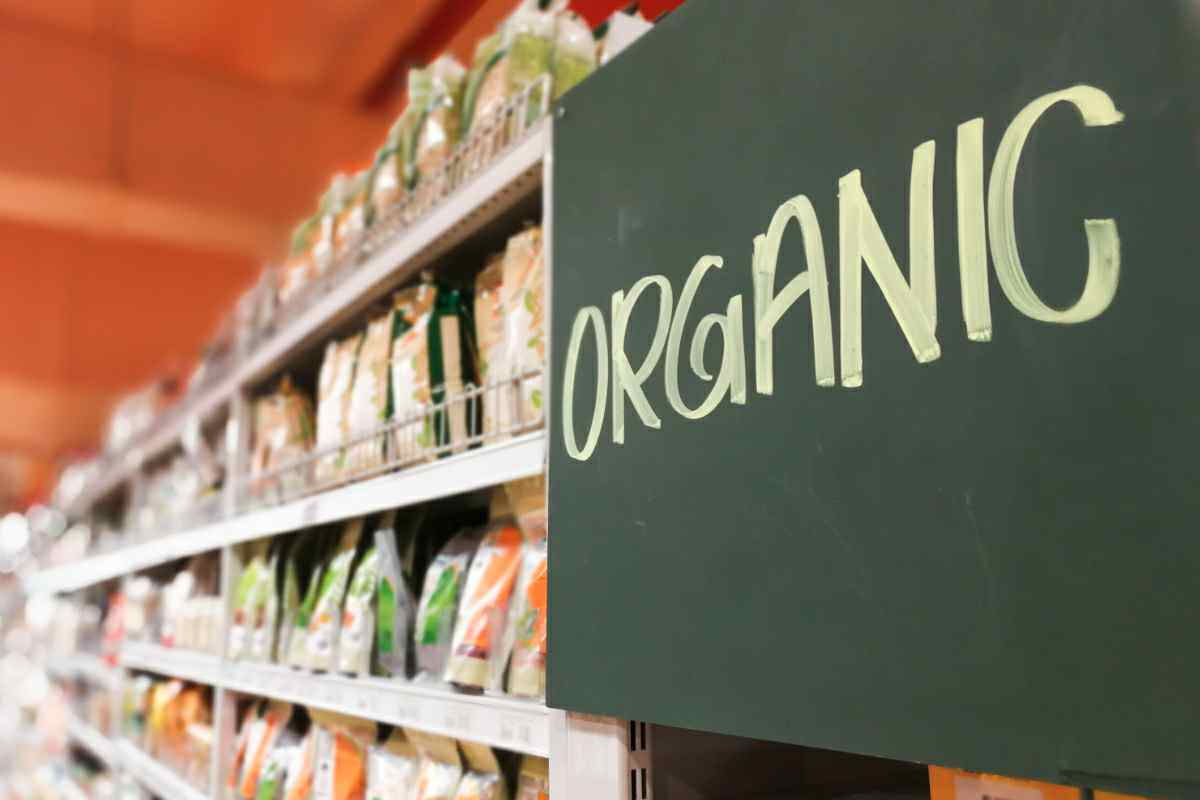 A shelf of a grocery store is shown with a sign the reads “ORGANIC” is featured, affixed to the grocery store shelf.