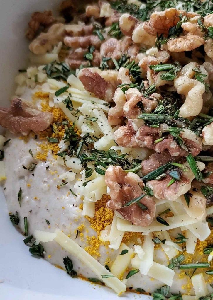A close up of sourdough add-ins that include walnuts, chopped herbs, grated cheddar cheese, and dry turmeric powder sitting atop fluffy dough.