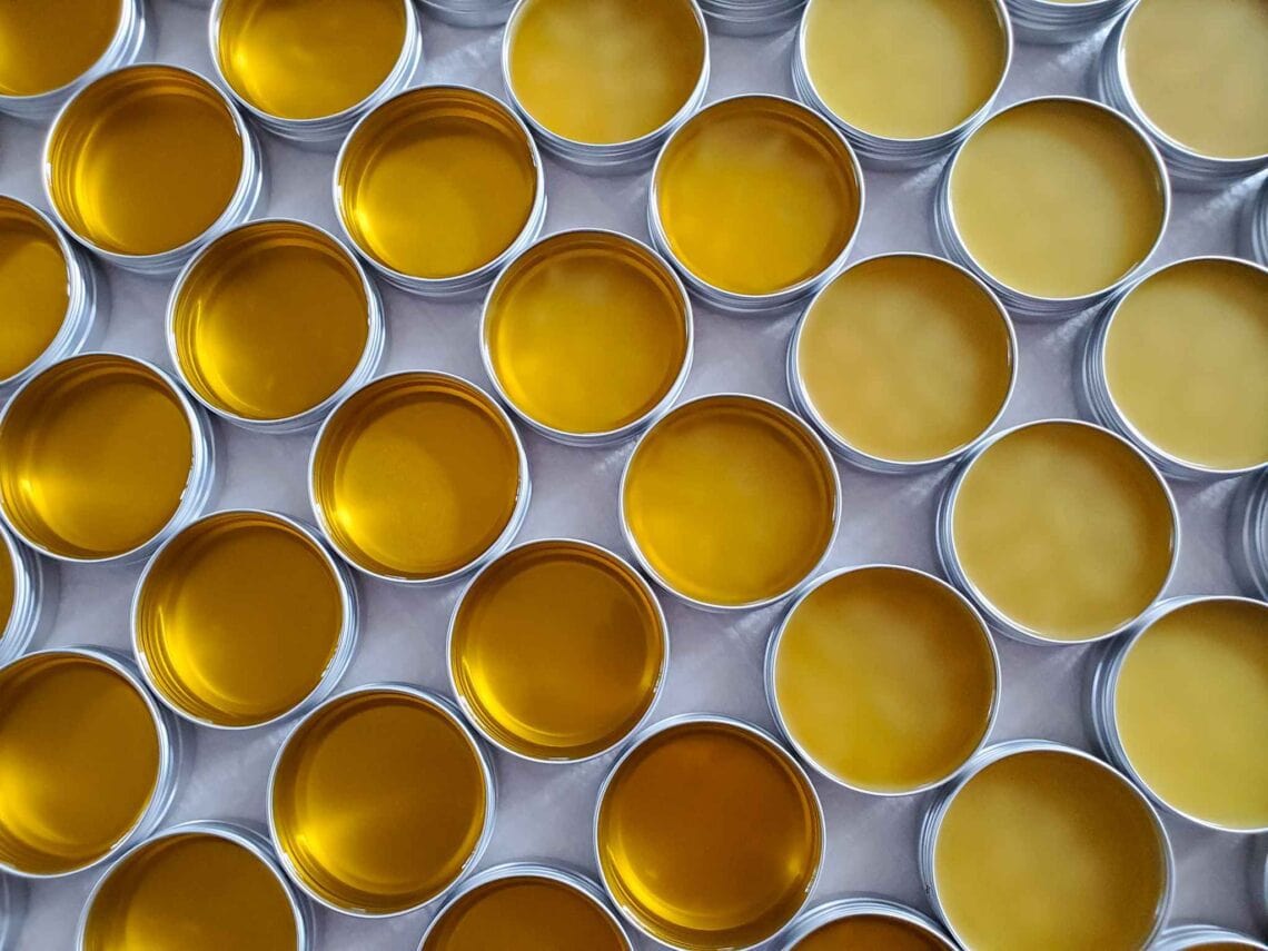 Many metal tins are arranged in a honeycomb pattern full of salve or balm in various stages of cooling as a few have cooled all the way to solid while a number of them are still liquid.