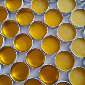 Many metal tins are arranged in a honeycomb pattern full of salve or balm in various stages of cooling as a few have cooled all the way to solid while a number of them are still liquid.