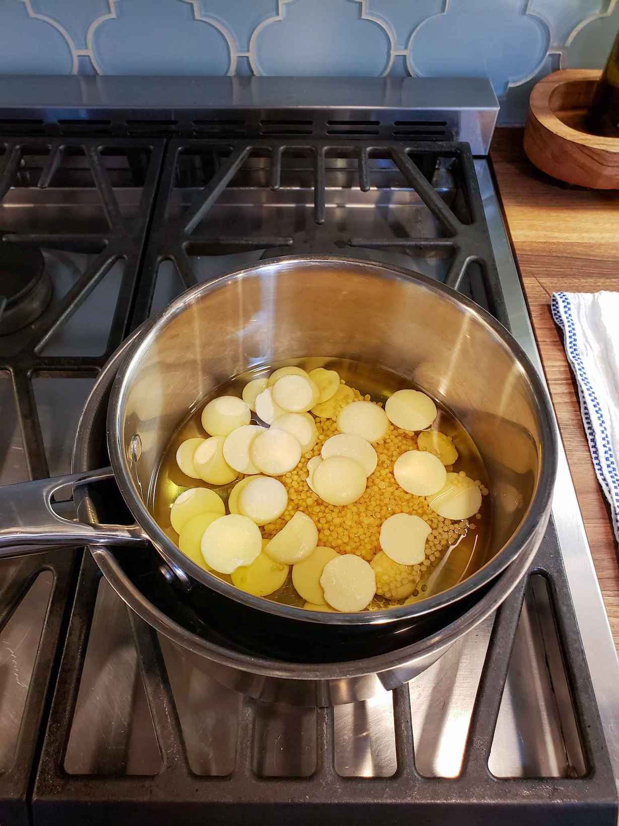 A small double boiler full of oil, cocoa butter wafers, and beeswax pastilles sits on the gas stovetop.
