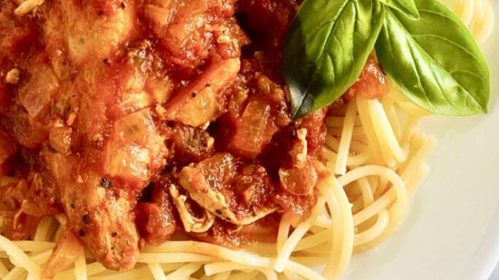 Chicken alla cacciatora over spaghetti on a plate with fresh basil leaves.