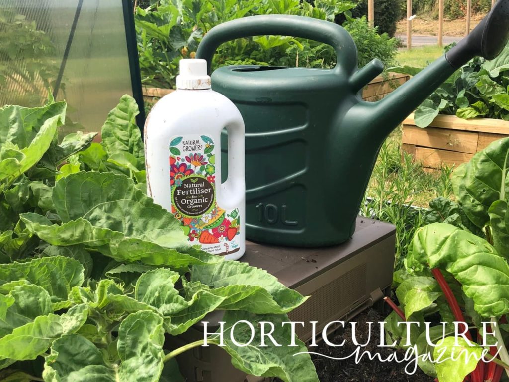 a white bottle of natural organic fertiliser and a green watering can