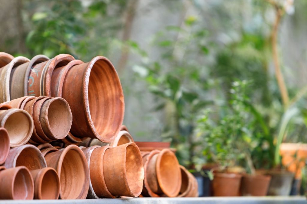 different sized ceramic pots stacked up and lying on their side outside with potted plants behind them