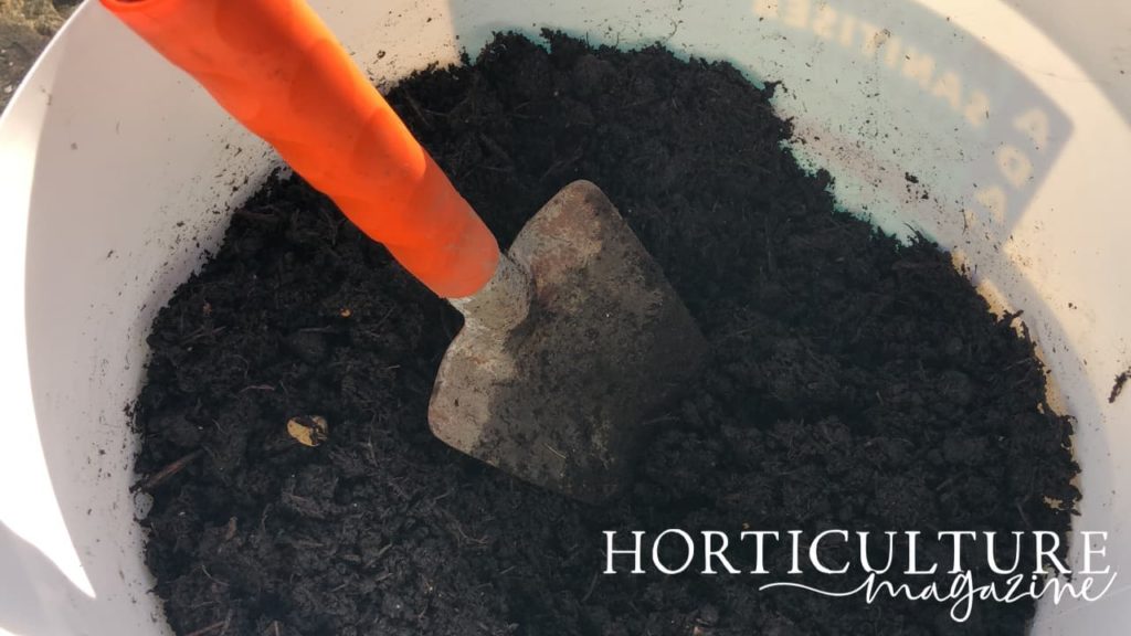 an orange handled trowel sat in a white container of compost