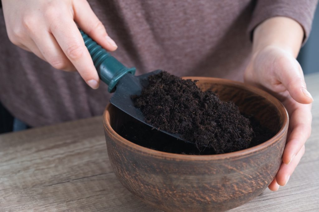 a trowel full of soil filling a small pot up with compost