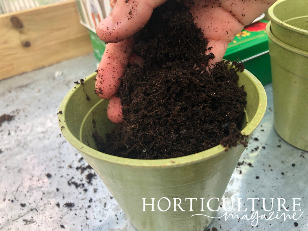 someone placing a handful of compost into a green container
