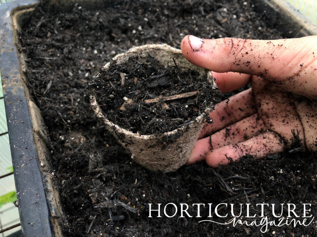 a pot full of soil ready for planting resting on top of a large container full of compost