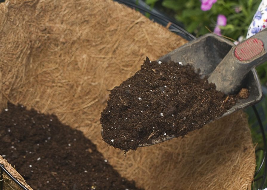compost being shovelled into a wicker hanging basket by a trowel