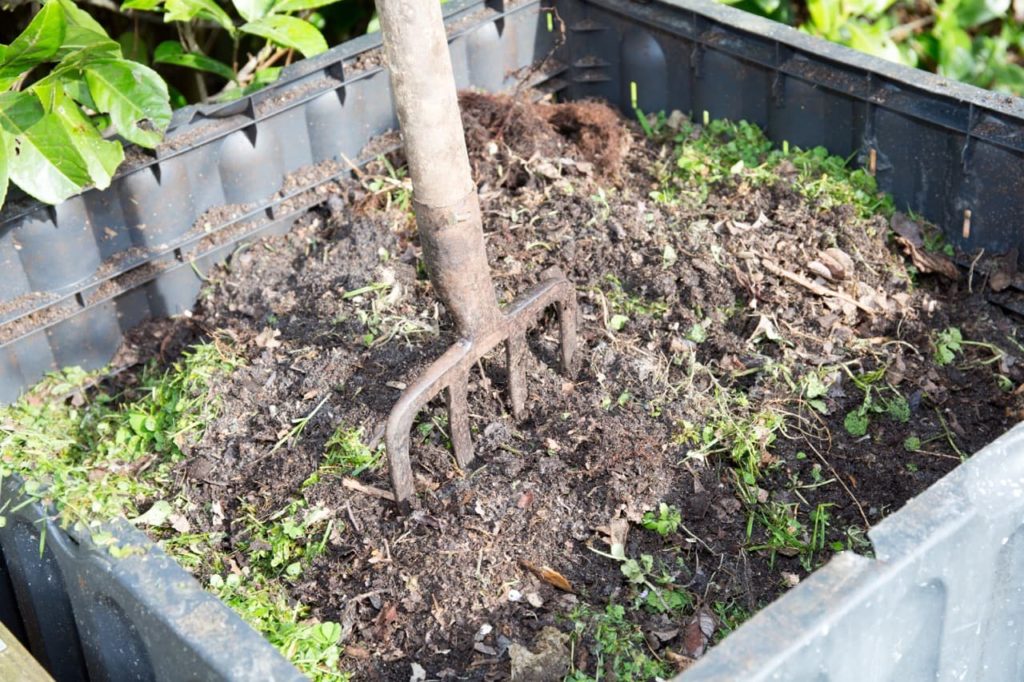 a black square compost bin with a large garden fork sticking out of it