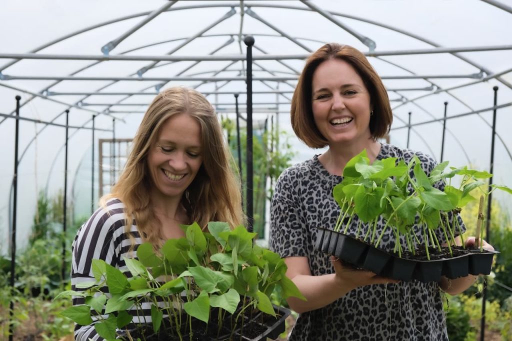 Lucy Hutchings and Kate Cotterill stood holding seed trays full of seedlings inside a polytunnel