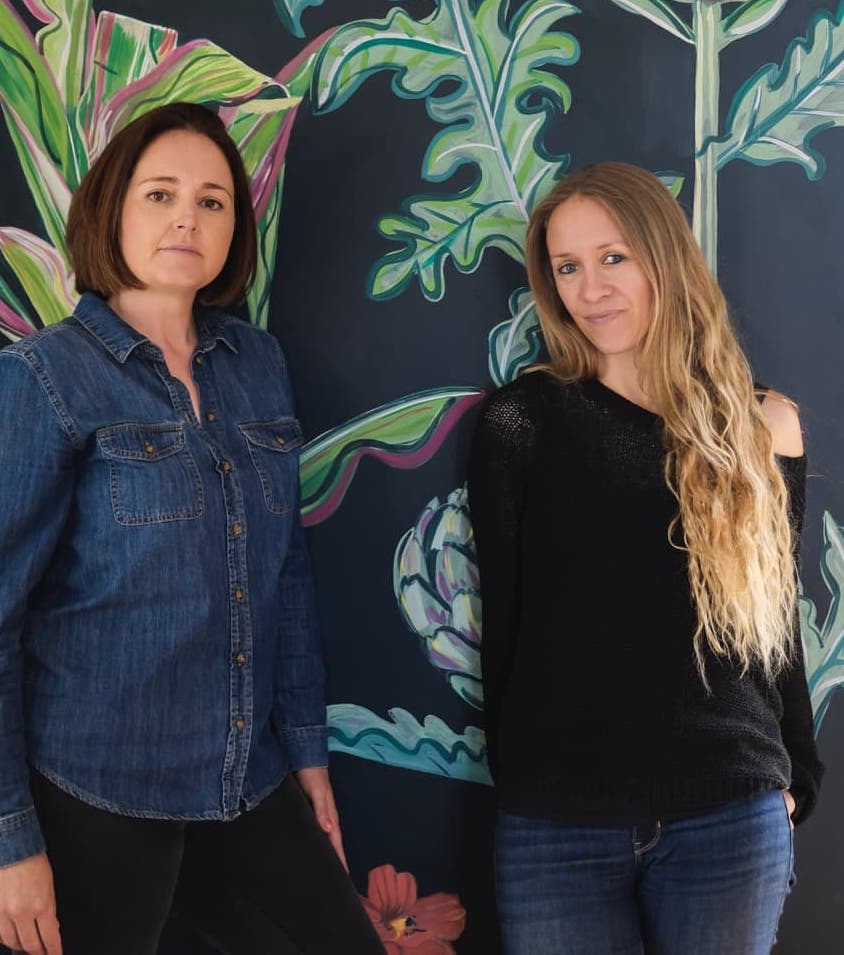 Kate Cotterill and Lucy Hutchings stood in front of a wall painted with flowers and plants