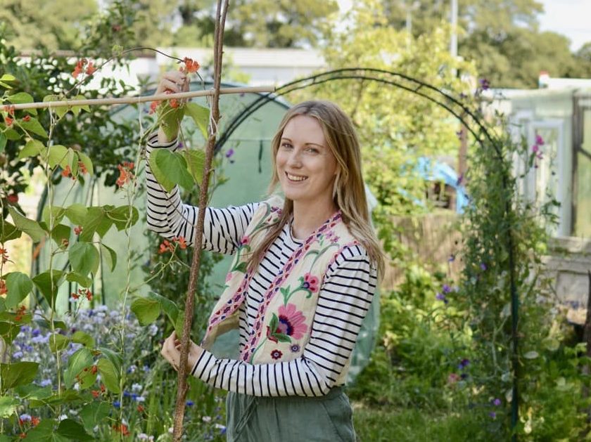 Emma Bailey tying orange flowering beans to a support in her allotment