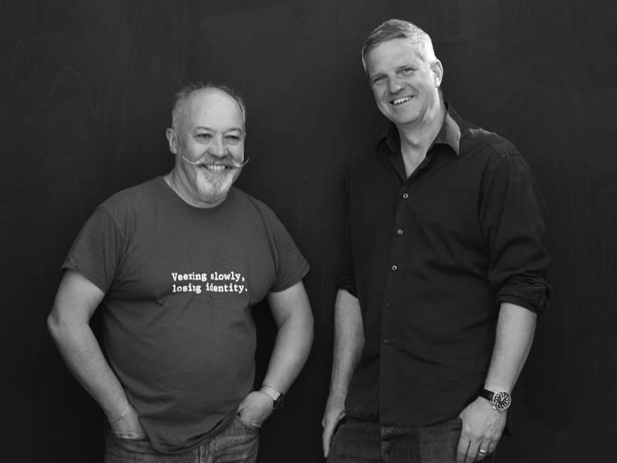 Todd and Gavin standing side by side in front of a black background