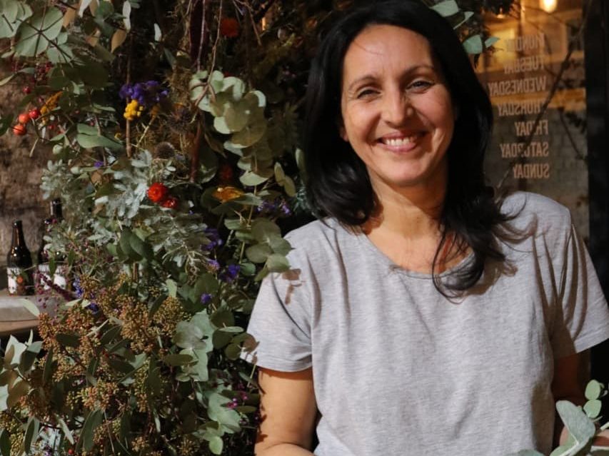 Sonya Patel Ellis smiling next to an arrangement of plants indoors